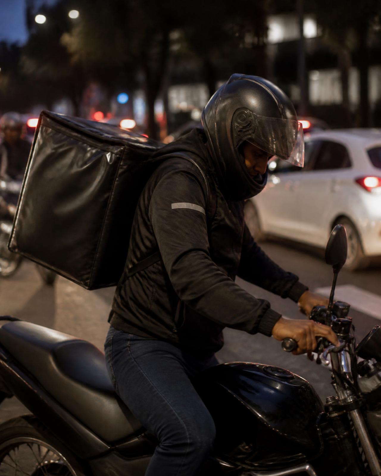 Entregador com bolsa de entrega subindo na moto no trânsito noturno